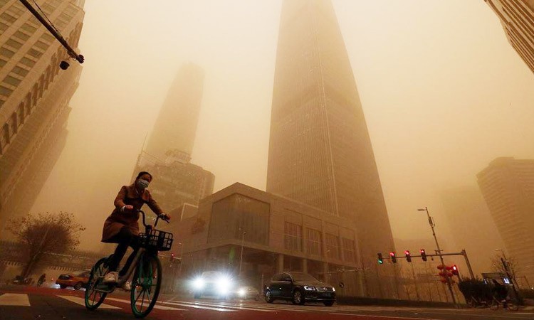 A cyclist and motorists move past office buildings amid a sandstorm during the morning rush hour in the central business district in Beijing. AP