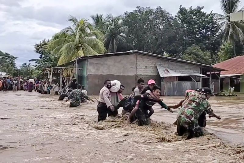 In this image made from video, soldiers and police officers assist residents to cross a flooded road in Malaka Tengah, East Nusa Tenggara province, Indonesia on April 5, 2021. Multiple disasters caused by torrential rains in eastern Indonesia have left dozens of people dead and missing and displaced thousands, the country's disaster relief agency said Monday. (AP/PTI Photo)