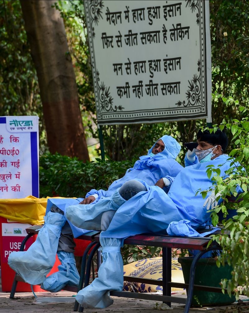 Health workers wearing PPE suits, sit on a bench during a break from cremation of COVID-19 victims, amid the rise in Covid-19 cases across the country, in Noida on April 29, 2021. (PTI Photo)