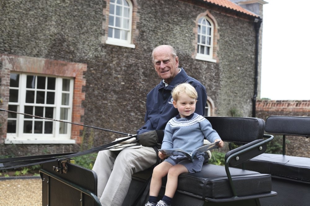 In this undated handout photo provided by the Duke and Duchess of Cambridge, Britain's Prince Philip sits with his great-grandson Prince George in England. Prince Philip, the irascible and tough-minded husband of Queen Elizabeth II who spent more than seven decades supporting his wife in a role that mostly defined his life, died on Friday, April 9, 2021. (Duke and Duchess of Cambridge via AP)