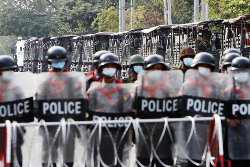 In this Friday, Feb. 19, 2021 file photo, military trucks with soldiers inside are parked behind police standing guard behind a road barricade in Mandalay, Myanmar. Ever since the military seized control of the country in February,?the conflict in Myanmar has become increasingly bloody. Security forces have killed more than 700 people, including a boy as young as 9. (AP File Photo)