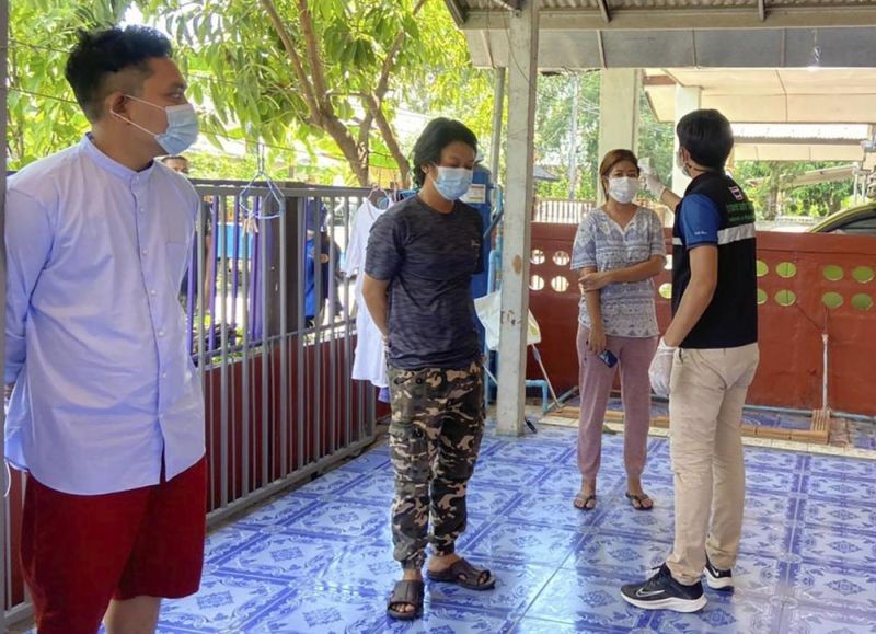 In this photo released by the San Sai District Administrative Office, a Thai officer checks the temperature of journalists working for Democratic Voice of Burma, at San Sai District in Chiang Mai province north of Thailand on May 9, 2021. Three senior journalists working for the online and broadcast news agency in Myanmar who fled after the military government ordered its operations to stop have been arrested by police in northern Thailand, their editor said Monday. (AP Photo)