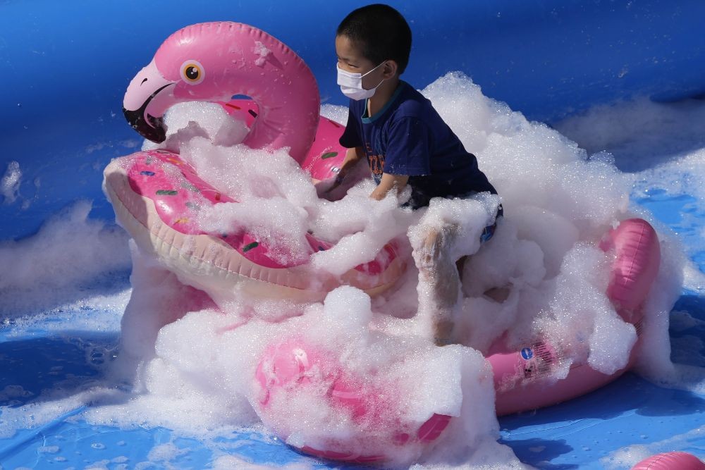 FILE PHOTO: Bejing: A child wearing a mask plays with a flamingo shaped balloon in bubbles during Children s Day at a mall in Beijing on Tuesday, June 1, 2021. China s ruling Communist Party said Monday it will ease birth limits to allow all couples to have three children instead of two in hopes of slowing the rapid aging of its population, which is adding to strains on the economy and society.AP/PTI