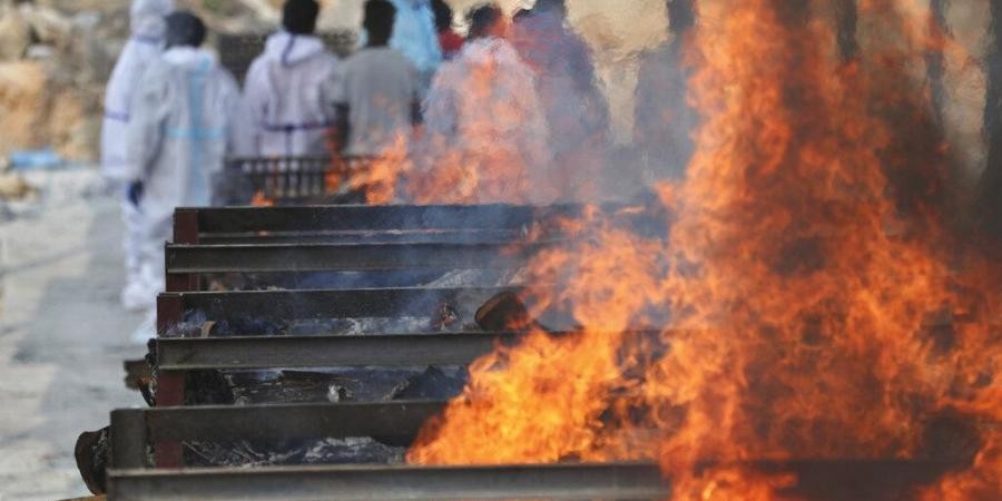 Family members perform last rites of a person who died of COVID-19 as funeral pyres of other victims burn at an open crematorium. (Photo | AP)