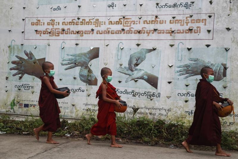 Buddhist novice monks wearing face masks walk past a COVID-19 awareness sign as they collect morning alms on July 15, 2021, in Yangon, Myanmar. (AP File Photo)