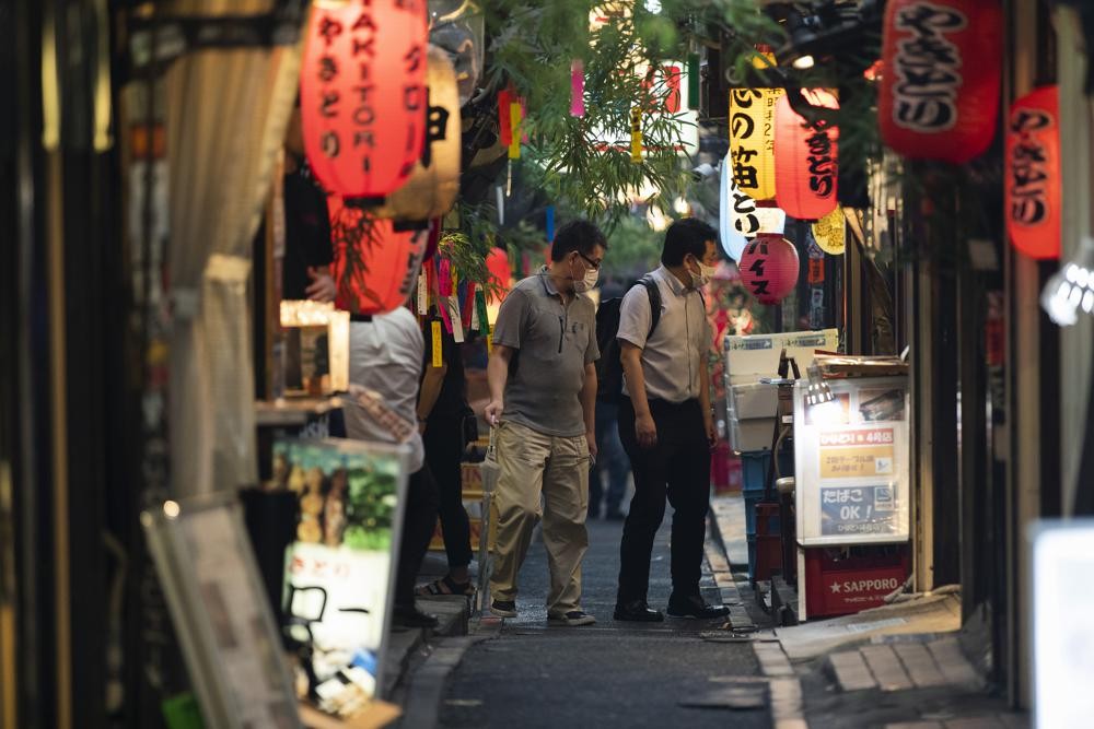 Men stop to check out a restaurant and bar in Tokyo on July 9, 2021. A state of emergency began Monday, July 12, 2021, in Tokyo, as the number of new cases is climbing fast and hospital beds are starting to fill just 11 days ahead of the Tokyo Olympics. (AP Photo/Hiro Komae)