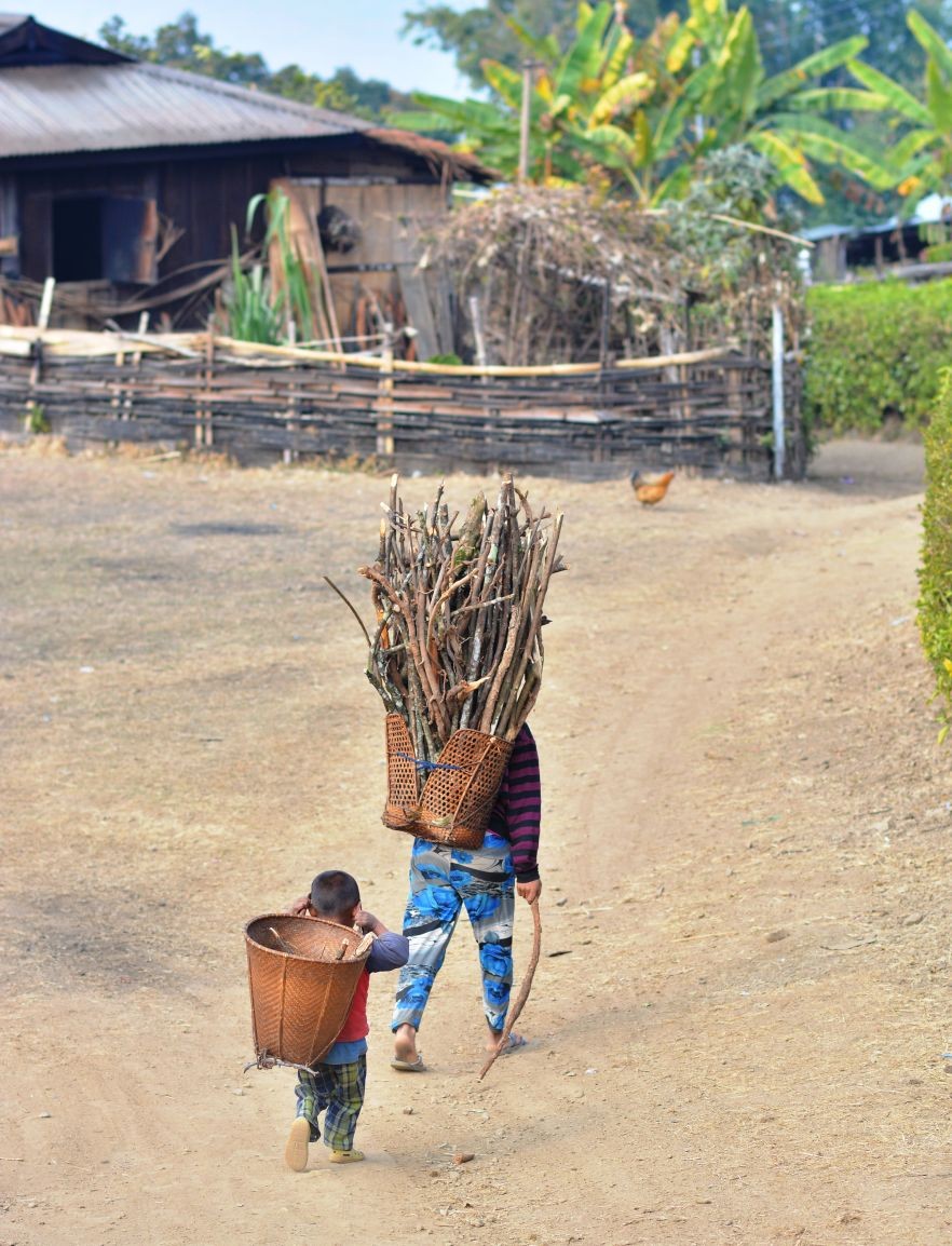 A woman carries firewood on the bamboo basket while a child follows her in a village in Nagaland. (Morung Photo)