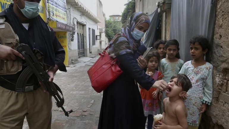 A police officer stand guard while a health worker administers a polio vaccine to a child in Peshawar. (AP photo)