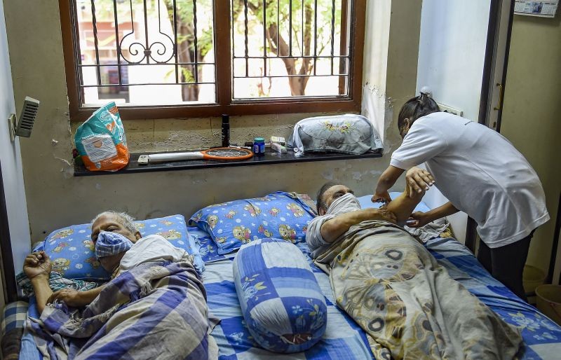 A healthcare volunteer inoculates an elderly man with COVID-19 vaccine dose at her home in Mumbai on August 5, 2021. Indian government has started door to door vaccination campaign for the sick and differently abled people who can't go out to take the vaccine. (PTI Photo)