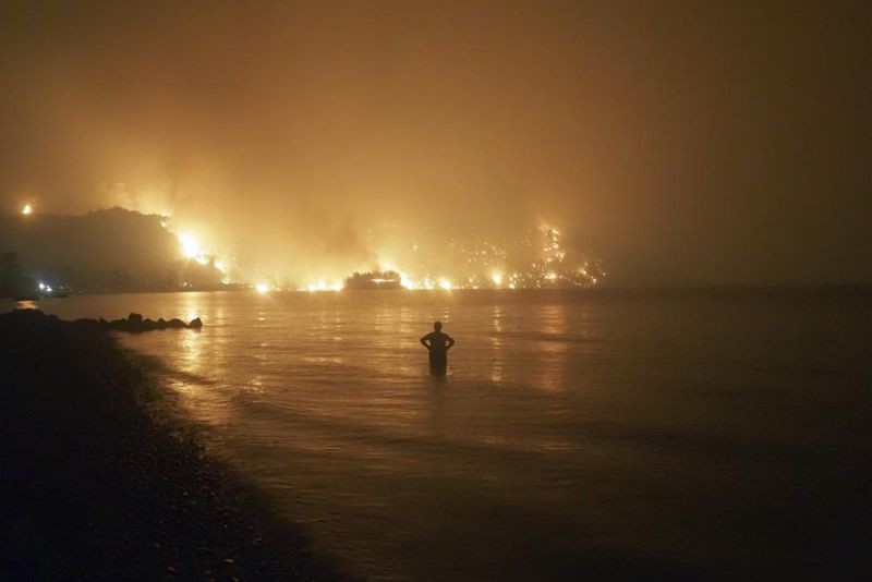 In this file photo dated Friday, Aug. 6, 2021, a man watches as wildfires approach Kochyli beach near Limni village on the island of Evia, about 160 kilometers (100 miles) north of Athens, Greece. A new massive United Nations science report is scheduled for release Monday Aug. 9, 2021, reporting on the impact of global warming due to humans. (AP Photo)