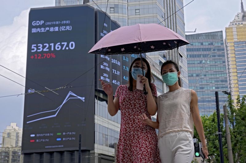 Women wearing face masks to help curb the spread of the coronavirus walk by an electronic billboard showing China s Gross Domestic Product (GDP) index on a commercial office building in Shanghai, China. ( AP/PTI Photo)