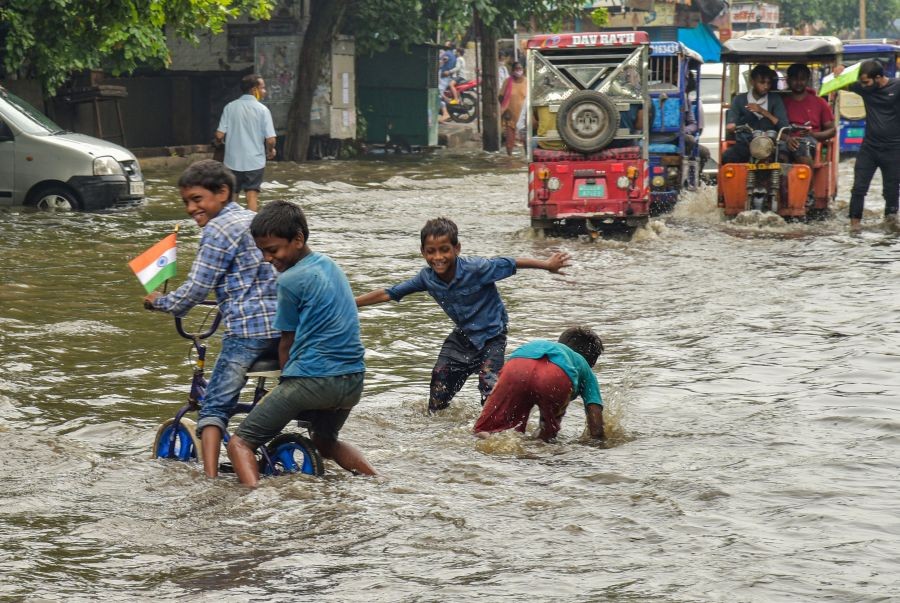 New Delhi: Children play in rain-water as vehicles wade through a waterlogged street after rain at Jahangirpuri area in New Delhi, Saturday, Aug. 21, 2021. (PTI Photo/Shahbaz Khan)
