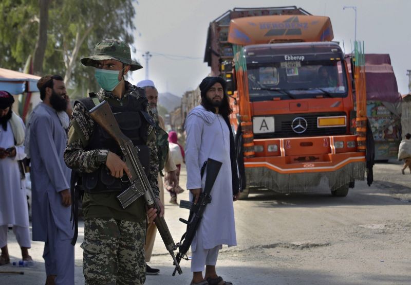 A Pakistani paramilitary soldier, front, and Taliban fighters stand guard on their respective sides while a truck moves to cross at a border crossing point between Pakistan and Afghanistan, in Torkham, in Khyber district, Pakistan on August 21, 2021. In the current situation of Afghanistan, pedestrian movement has limited in Torkham border, only stranded people in both sides and trucks taking goods to Afghanistan can passes through this border point. (AP/PTI Photo)