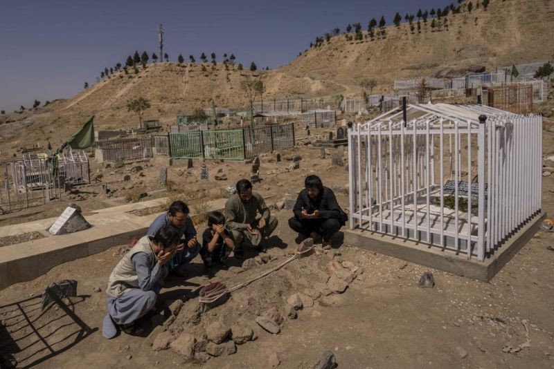 In this Monday, Sept. 13, 2021 file photo, the Ahmadi family pray at the cemetery next to family graves of family members killed by a US drone strike, in Kabul, Afghanistan. Sorry is not enough for the Afghan survivors of an errant U.S. drone strike that killed 10 members of their family, including seven children. On Saturday, Sept. 18, they demanded Washington investigate who fired the drone and punish the military personnel responsible for the strike, said Emal Ahmadi, whose 3-year-old daughter Malika was killed on Aug. 29 when the U.S. hellfire missile struck his elder brother's car. (AP File Photo)