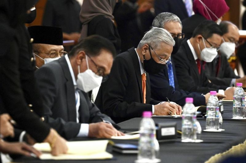 In this photo released by Malaysia's Department of Information, Malaysian Prime Minister Ismail Sabri Yaakob, center, and opposition leader Anwar Ibrahim, left, sign documents during a ceremony at Parliament at the parliament house in Kuala Lumpur, Malaysia on Sept. 13, 2021. Ismail signed an unprecedented cooperation pact with the main opposition bloc led by Anwar. The deal will prevent any bid to undermine Ismail's rule ahead of general elections due in two years. (AP File Photo)