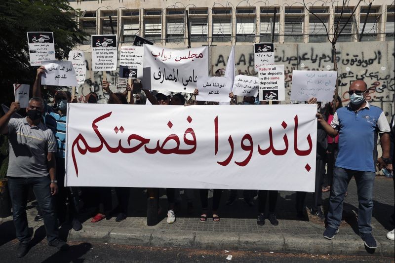 Customers hold a banner with Arabic that reads: "Pandora (Papers) exposed you," during a protest in front of the Central Bank in Beirut, Lebanon on October 6, 2021. Dozens of Lebanese gathered outside a bank in Beirut's downtown demanding that they be allowed to withdraw their deposits that have been blocked amid Lebanon's severe financial and economic crisis. (AP/PTI Photo)