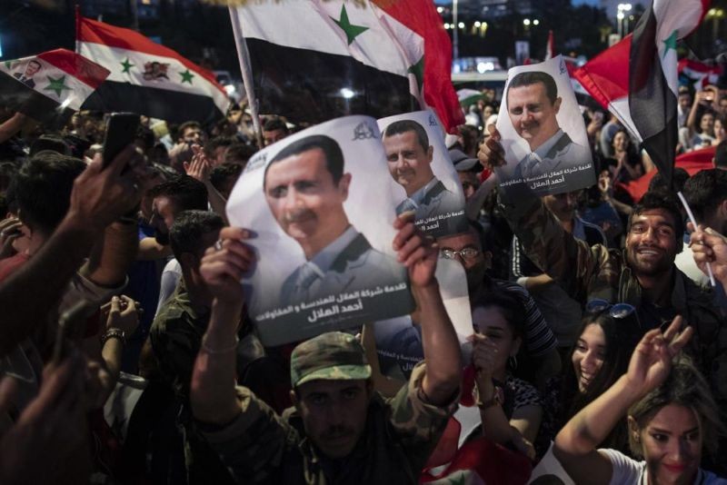 In this May 27, 2021 file photo, Syrian President Bashar Assad supporters hold up national flags and pictures of Assad as they celebrate at Omayyad Square, in Damascus, Syria. Jordan’s King Abdullah received a call from Syrian President Bashar Assad, Sunday, Oct. 3, 2021, the first between the two leaders after a decade of strained relations over Syria's civil war. (AP File Photo)