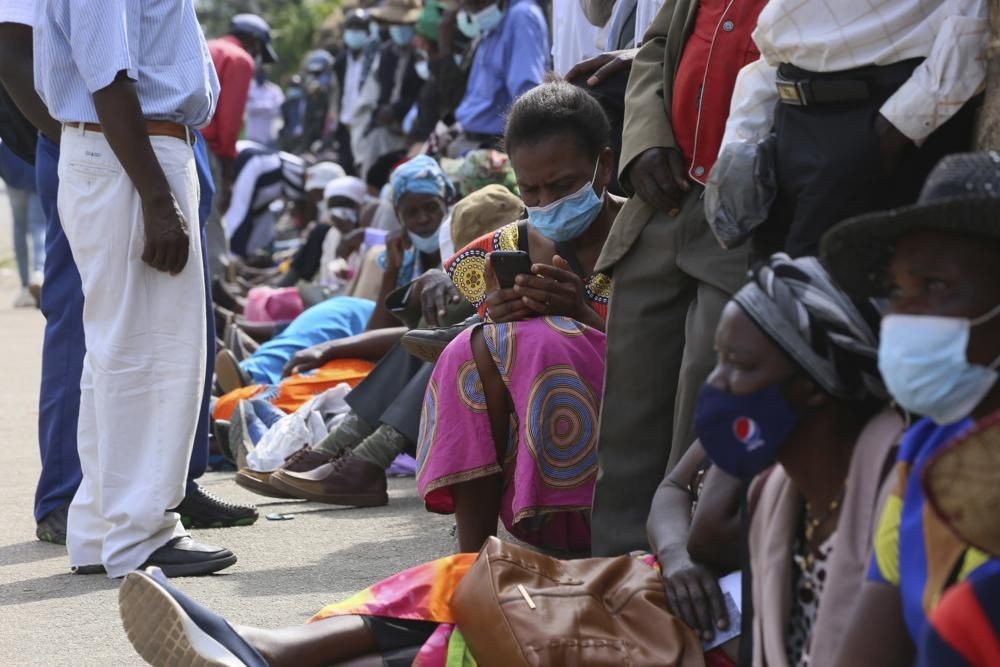 A woman reads messages on her mobile phone while waiting in a bank queue in Harare, Zimbabwe on Monday, Dec. 13, 2021. In Zimbabwe and other African nations, the virus's resurgence is threatening the very survival of millions of people who have already been driven to the edge by a pandemic that has devastated their economies. When putting food on the table is not a given, worries about whether to gather with family members for the holiday or heed public announcements urging COVID-19 precautions take a back seat. (AP Photo/Tsvangirayi Mukwazhi)