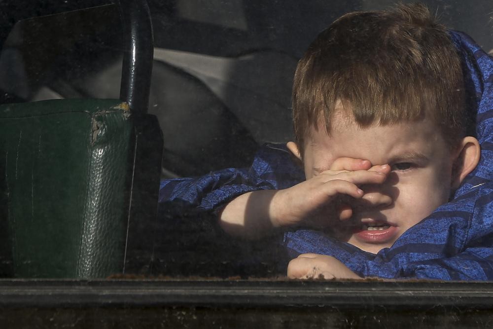 A boy waiting to be evacuated to Russia looks through the window of a bus, in Donetsk, the territory controlled by pro-Russian militants, eastern Ukraine, Saturday, Feb. 19, 2022. On Friday, separatist authorities in eastern Ukraine announced a mass evacuation of women, children and older adults to neighboring Russia. The moves have have fueled Western fears that Moscow could use the latest violence in eastern Ukraine as a pretext for an invasion. (AP Photo/Alexei Alexandrov)